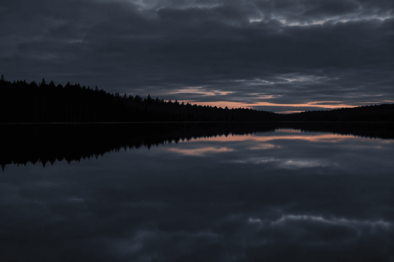 A Finnish forest lake at dusk, still water reflecting a clouded sky